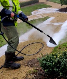 Operator usuwa chwasty metodą gorącej wody na dużym placu